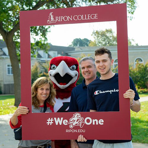 Ripon College student and his parents pose for a picture with Rally the Red Hawk at Family Weekend